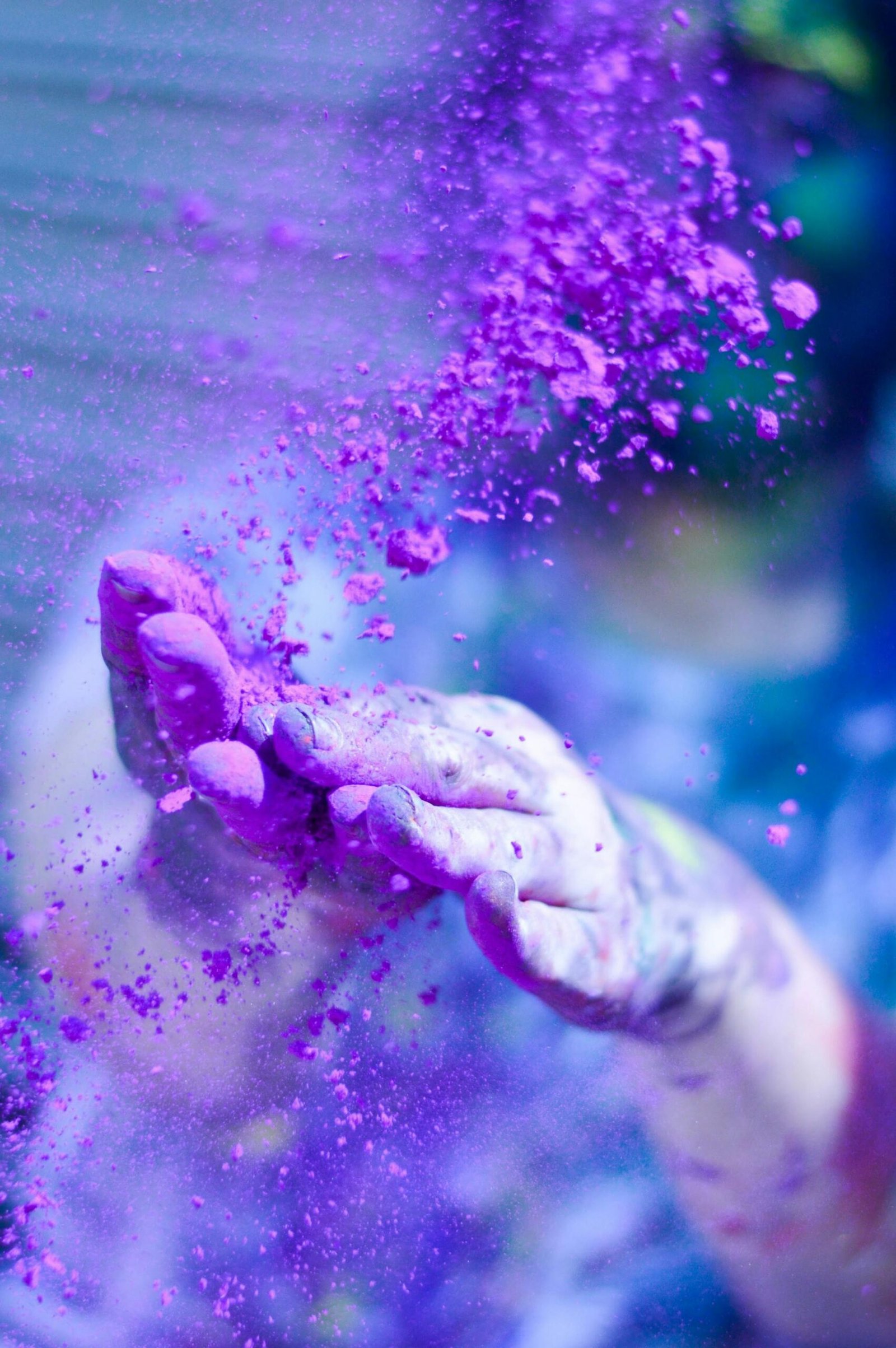 Quienes-Somos Close-up of hands throwing vibrant purple powder outdoors, capturing motion and color.